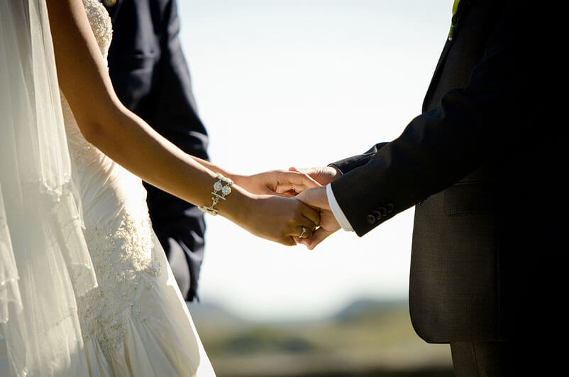 Närbild på brudens och brudgummens händer under vigseln.